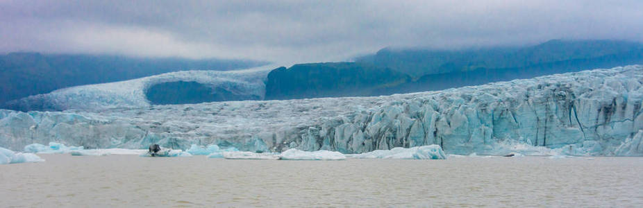 在南冰岛巨大的 Vatnajokull 冰川的手臂上的 Fjallsarlon 冰川泻湖上的小船游的蓝色冰