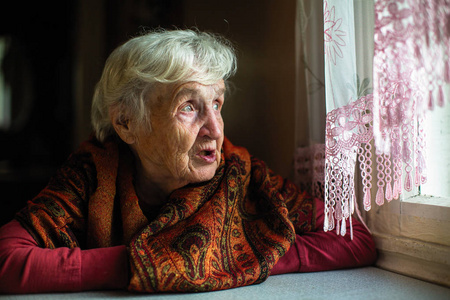 坐在房子里的老年妇女的肖像望着窗外
