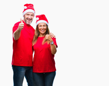 中年拉美裔夫妇穿着圣诞帽子在孤立的背景做愉快的拇指手势与手。批准表达式看着相机显示成功