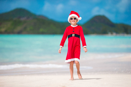 热带海滩上圣诞老人帽的可爱小女孩