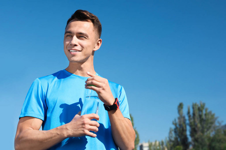 阳光明媚的日子里, 年轻的运动男子在体育场拿着一瓶水。文本的空间