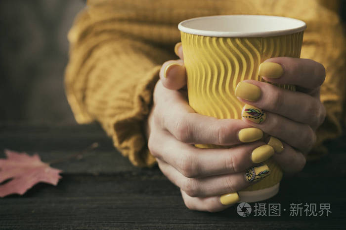 女性的手, 有一个明亮的修指甲和一个黄色的纸杯。特写