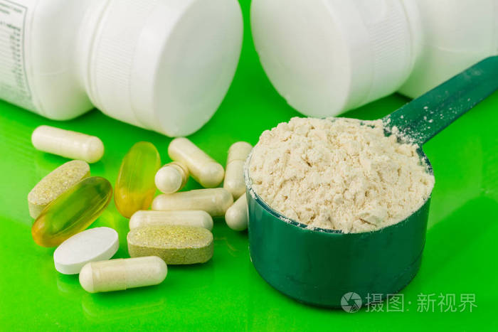 混合的天然食品补充药片和蛋白粉在绿色背景上的塑料勺