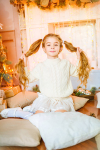 可爱的小女孩与金发长卷发在一个光针织毛衣由节日壁炉与花环和蜡烛