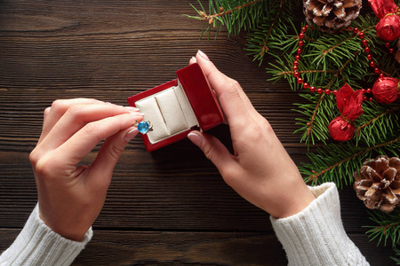 在女性手中木背景上的圣诞装饰品的订婚戒指