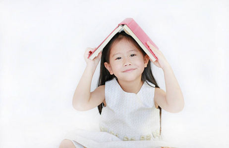 纵向小亚洲女孩地方精装书在她的头上, 看着相机在白色背景