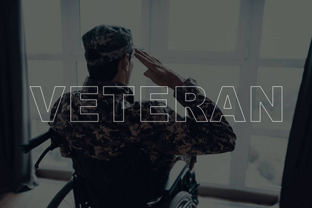 退伍军人。坐在轮椅上的残疾人。男人在窗户前。男人看着窗户。人是战士。身穿军服的士兵男人在敬礼。位于客厅里的男人