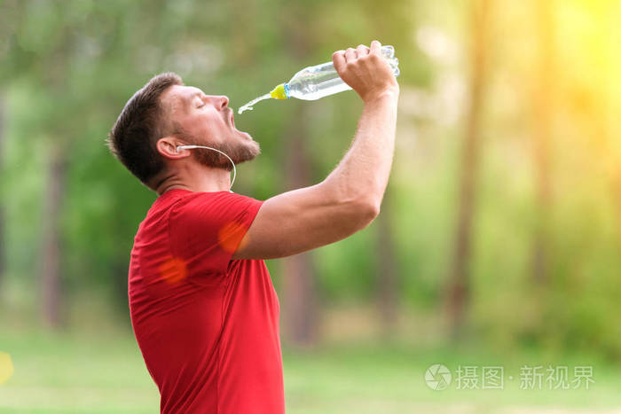 健身男子从瓶子里喝水.口渴的运动员在剧烈运动后喝冷饮
