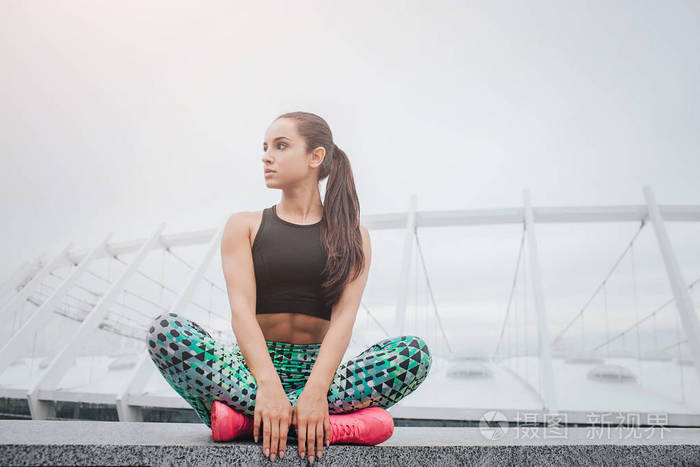 美丽而迷人的年轻女运动员坐在一起, 双腿交叉, 用手抱着腿.