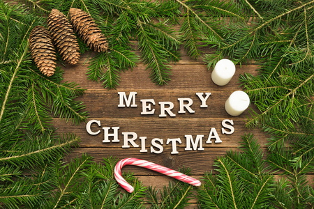 在木制的背景下写上圣诞快乐。冷杉树枝棒棒棒和蜡烛的框架