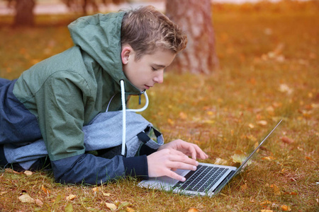 少年与笔记本电脑躺在秋天的公园的草坪上