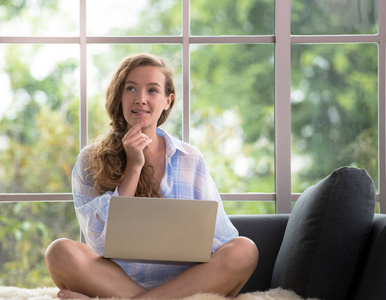 健康的年轻妇女坐在沙发上使用笔记本电脑看起来轻松舒适