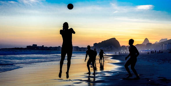 跳跃的人在里约热内卢科帕卡巴纳海滩上的美丽的日落背景玩沙滩足球的剪影