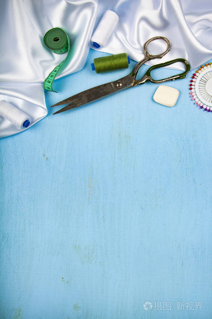 在蓝色木制背景上缝制配件.白色缎布, 剪刀和螺纹.文本位置