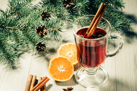 一杯圣诞美酒, 肉桂, 八角和丁香在木背景上的白色饼干, 橘子片, 天然冷杉树枝和锥。色彩调理效果