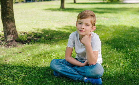 7岁的男孩在公园里放松。穿着休闲装坐在草地上的男孩