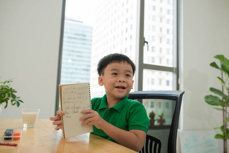 可爱的微笑的亚洲男孩做作业, 而坐在办公桌, 教育概念