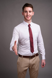 工作室拍摄年轻英俊的商人穿着白色衬衫和红色领带反对灰色背景