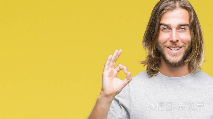 长头发的年轻英俊的人在被隔绝的背景微笑正面做 ok 标志用手和手指。成功表达式