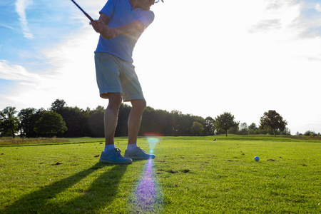 老人打高尔夫球在绿色草坪上在德国南部日落与阳光束闪耀