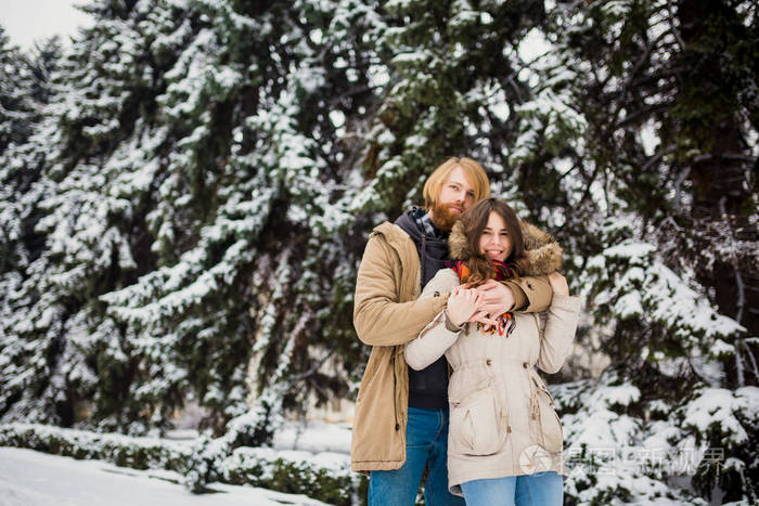 年轻的高加索男孩和女孩在爱异性恋夫妇有一个约会在户外的冬季公园的背景下, 一个雪针叶树站在一个拥抱。男人拥抱妇女情人节