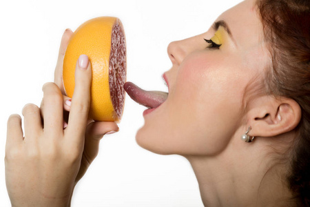 年轻的红头发的女人一个白色的背景柚子。健康饮食概念