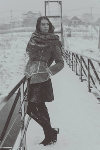 这位俄罗斯美女站在桥上在冬天的雪，黑色和白色