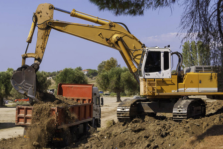 黄色车身施工现场的黄色挖掘机将土壤装进红色自卸车的车身照片