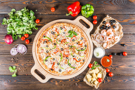 大比萨饼与海鲜, 虾和橄榄在一个圆形的切菜板上的一个黑暗的木制背景。食品配料