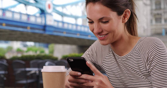 年轻的高加索女士与咖啡杯短信在电话坐在塔桥