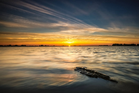 沿着弗莱沃兰边缘湖泊的日落。漂浮的浮木被冲到了海岸上, 可以看到平坦的荷兰波德景观