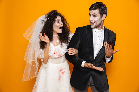 愉快的僵尸夫妇新郎和新娘穿着婚纱服装和万圣节化妆笑在黄色背景