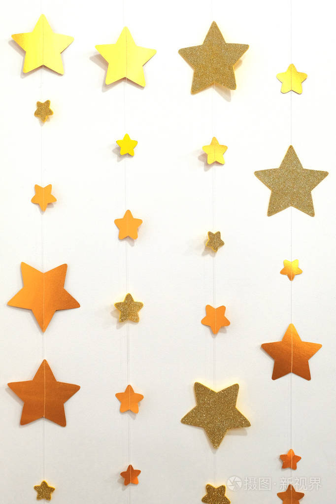 一根白色的线上挂着金色星星的纸花环。设计背景的装饰在房间里。圣诞墙面装饰。垂直图像