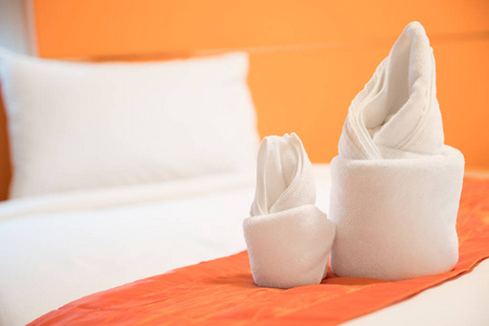 在橙色房间的床上准备的折纸毛巾