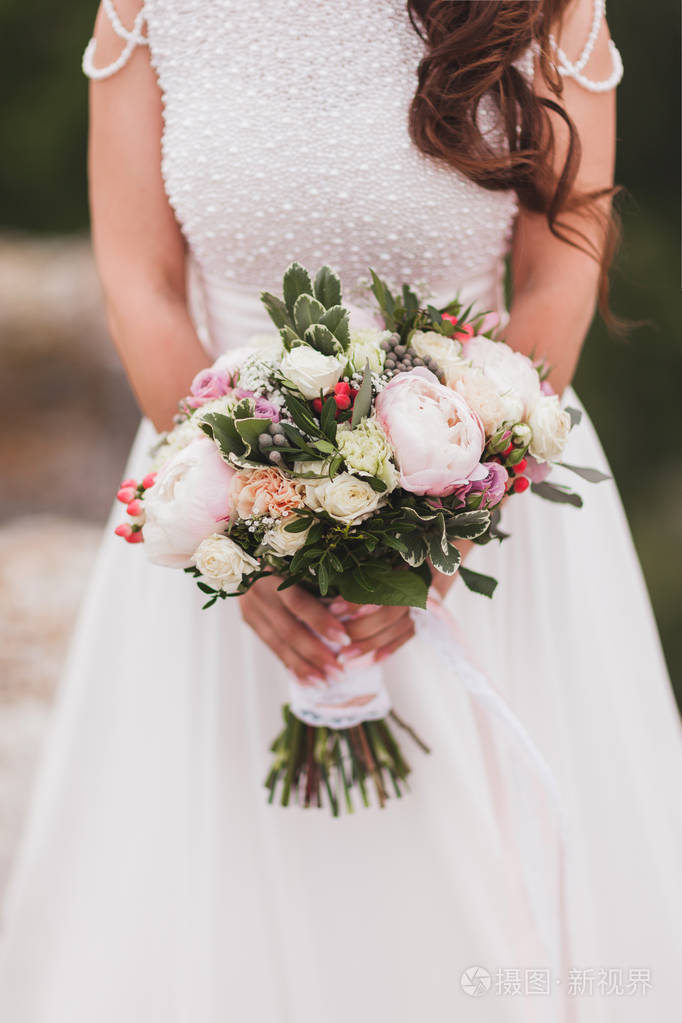 新娘手拿着美丽的花束在经典风格与牡丹和白色丝带