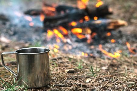 铁杯热奶茶站在靠近火的圆木上。野生的概念的旅程