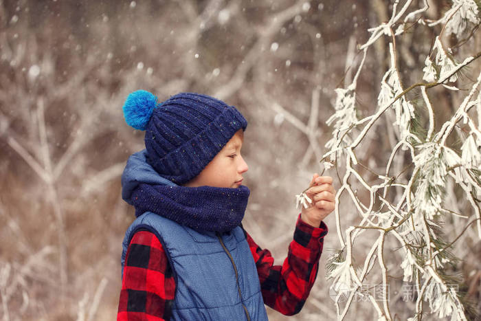 在森林里冬季散步时戴着温暖帽子和围巾的男孩