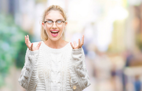 年轻漂亮的金发女人戴着眼镜在孤立的背景下疯狂和疯狂的呼喊和挑衅的表达和手臂举起。挫折概念