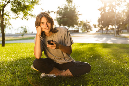 在公园里坐在草地上用电话聊天的快乐的年轻人的形象