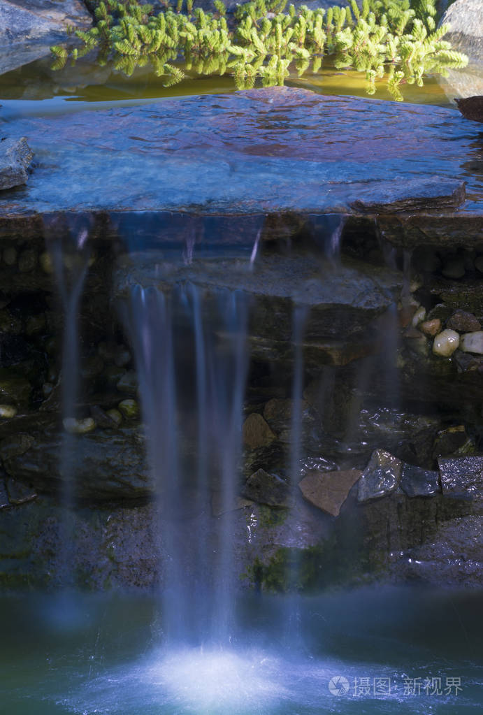 在一个园林绿化的院子池塘里, 水从一个小瀑布上掉了下来