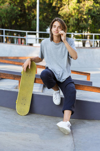 英俊的年轻滑板手坐在公园里的滑板的图像