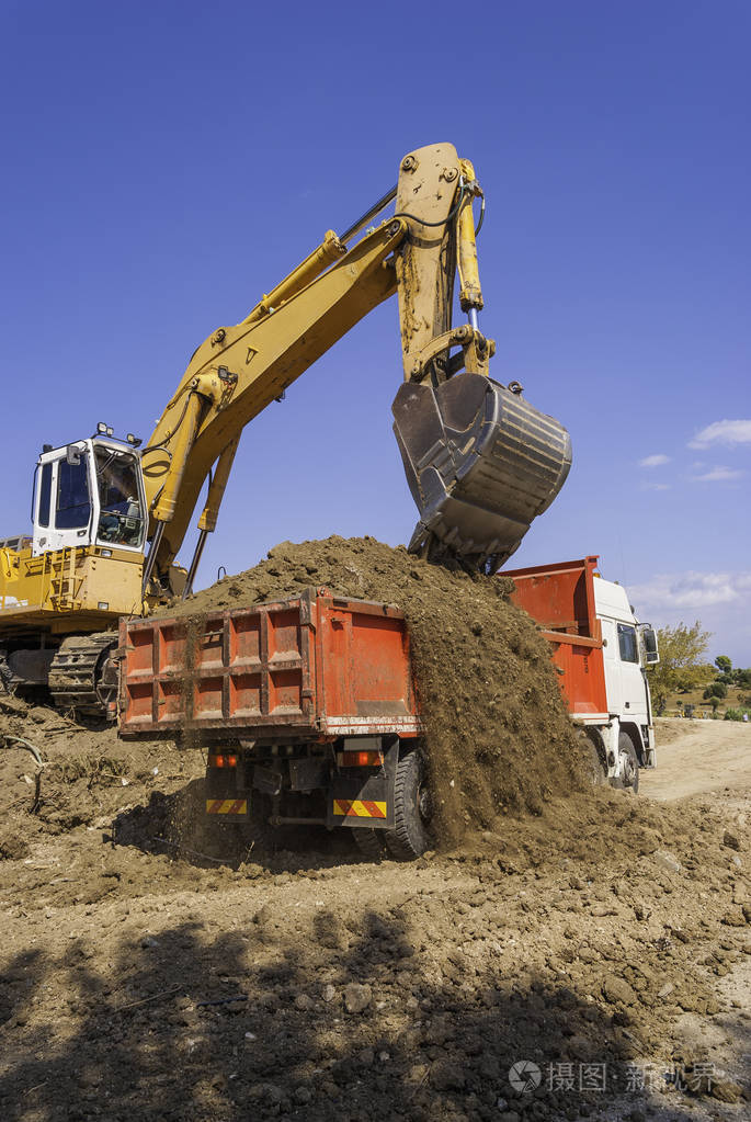 施工现场的黄色挖掘机将土壤装进红色自卸车的车身
