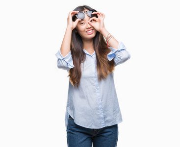年轻的亚洲妇女戴着太阳镜在孤立的背景下做 ok 手势用手微笑, 眼睛看通过手指与愉快的面孔