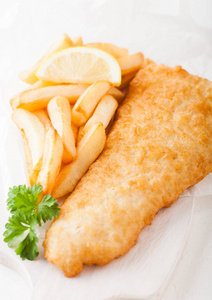 传统的英国鱼和芯片在切菜板和柠檬片在白色石头背景