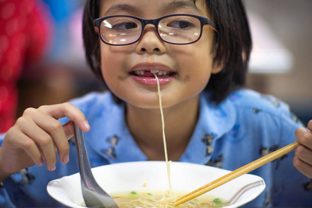可爱的小女孩吃面条与有趣的脸照片