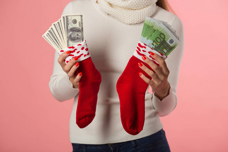 美丽的年轻女孩在冬季帽子与红色袜子与钱在一个粉红色的背景