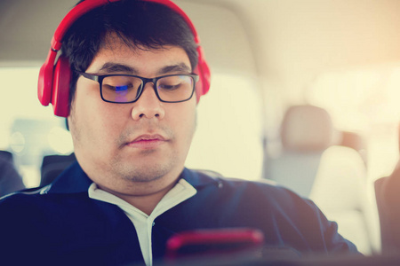 放松年轻的胖子在汽车上听音乐的智能手机与红色耳机。上下班的概念愿望城市生活专注旅程动力