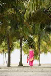 年轻女子走在沙滩上，在椰子树下，