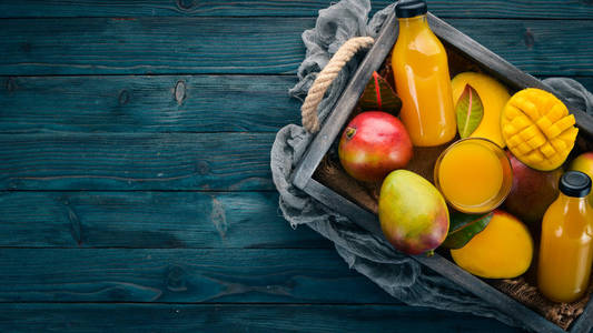 芒果和果汁放在木箱里。在一个木制的背景。热带水果。顶部视图。可用的复制空间