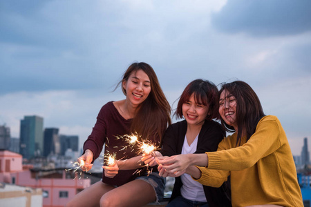 快乐组亚洲女孩朋友享受和玩烟火在屋顶党在黄昏日落, 节日庆典节日, 十几岁的生活方式, 自由和乐趣